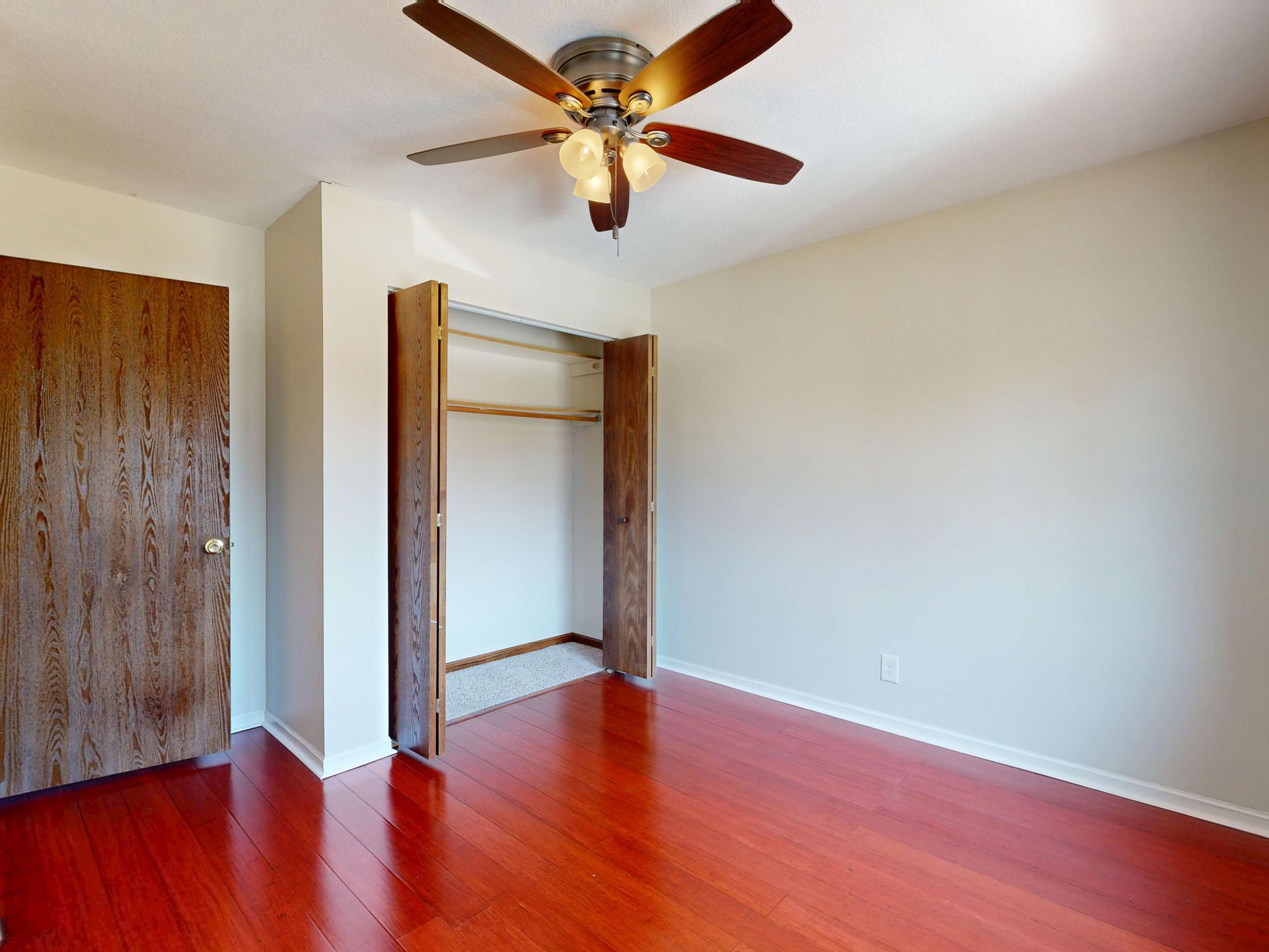Spacious empty room featuring a wooden floor, ceiling fan, and open closet.