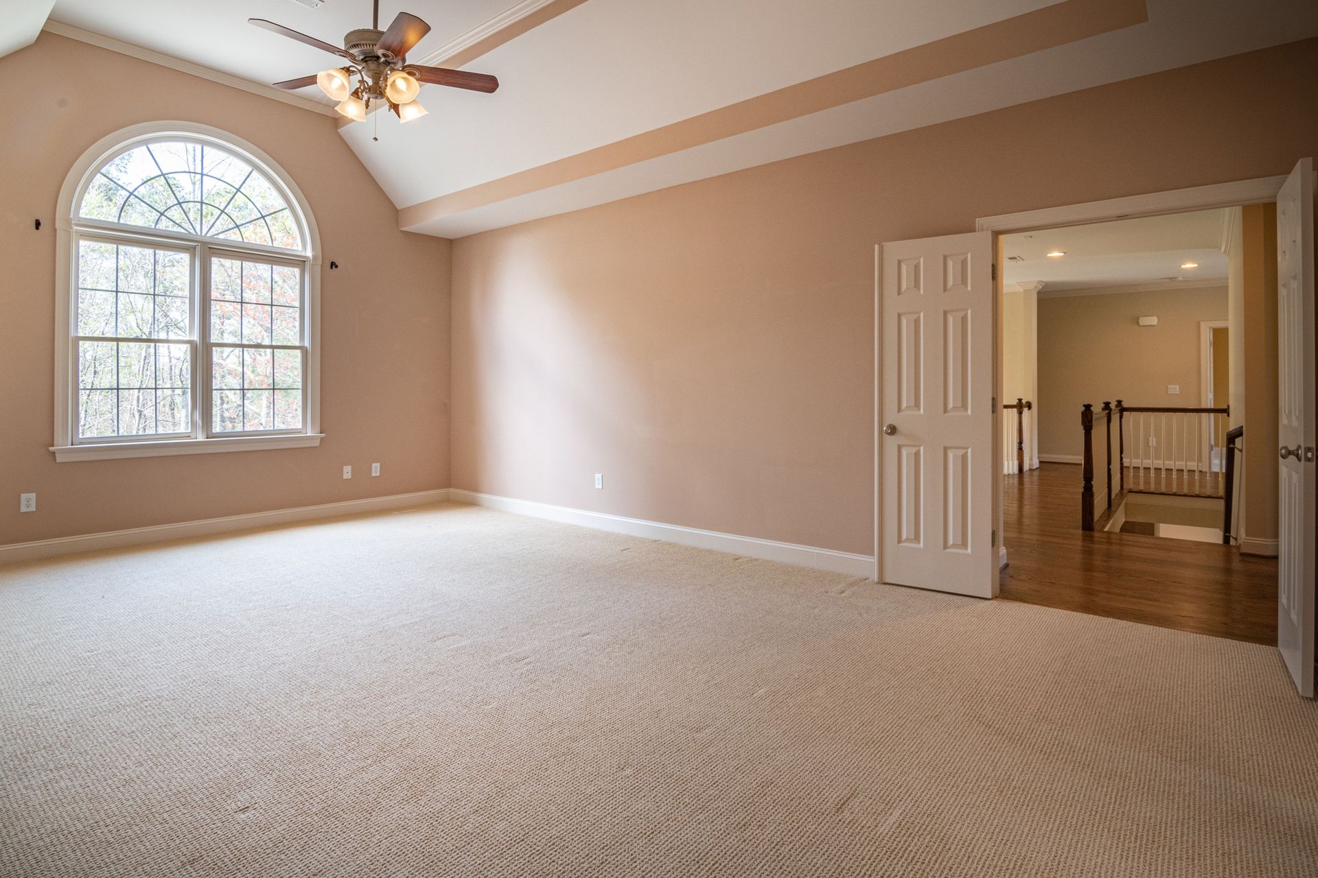 Bright empty room with beige walls, carpet flooring, and a large window showcasing modern architecture.
