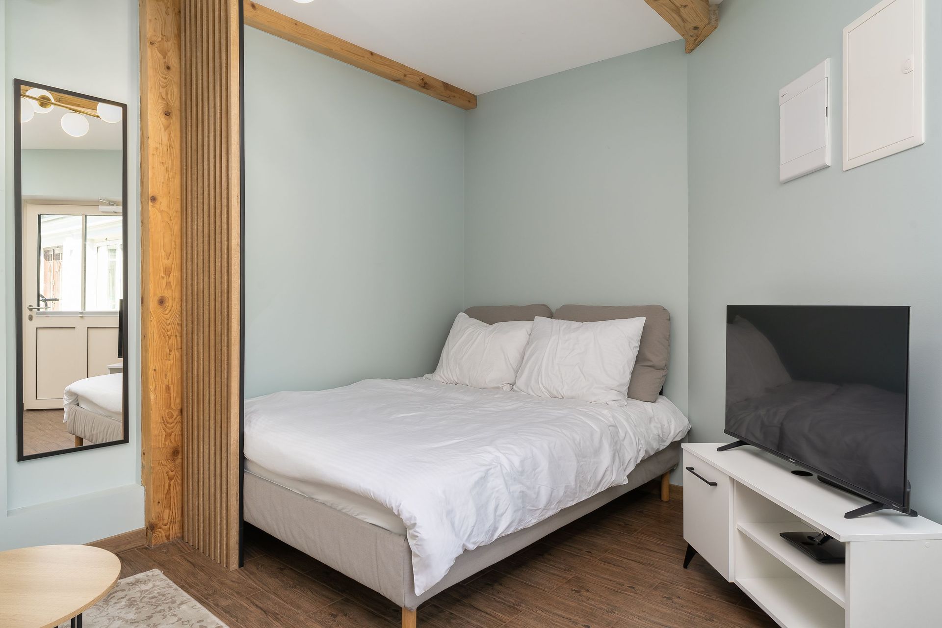 Modern minimalist bedroom with a cozy bed, wood accents, and a flat-screen TV.